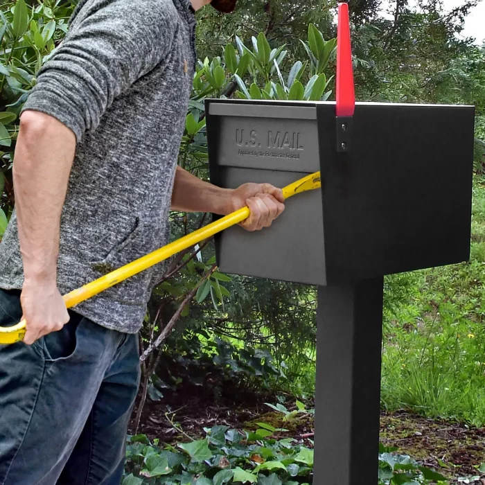 A man using a yellow crowbar to open a black metal mailbox